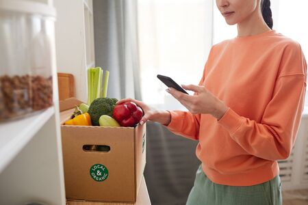 Close-up of young woman typing a message on her mobile phone while standing near the cardboard box...