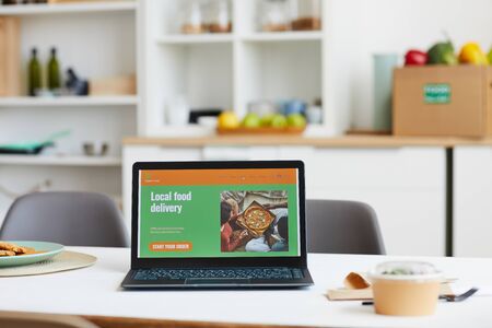 Laptop computer with website of food delivery on the screen on the table in the kitchen