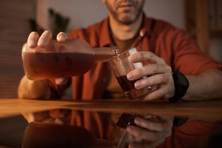 Close-up of young man sitting at the table and pouring alcohol from the bottle into the glassの写真素材