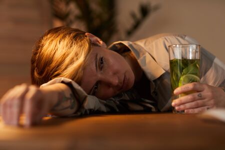Young drunk woman lying on the table she drinking alcohol cocktail