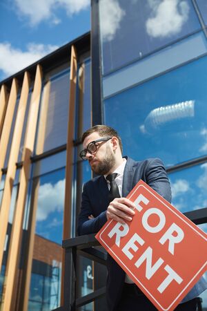 Man in suit working as a realtor he standing near the office building outdoors and holding placardの写真素材