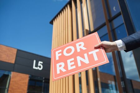 Close-up of businessman holding placard For Rent against the new modern office buildingの写真素材