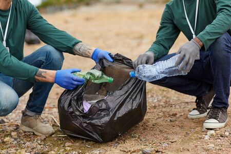 Close-up of people putting the garbage into the big black bags outdoors