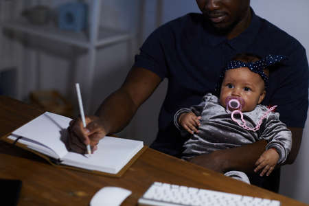 African father making notes in note pad while sitting at the table with baby on his kneesの写真素材
