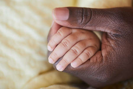 Close-up of African male hand holding little hand of newbornの写真素材