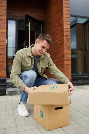 Young man happy because he getting his parcels he sitting outdoors and opening themの写真素材