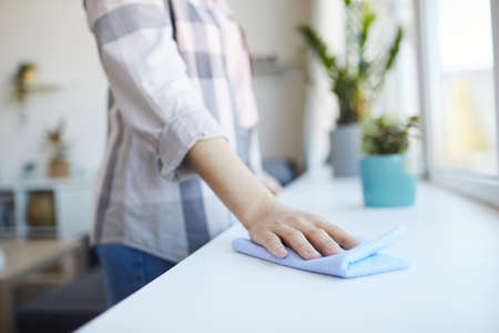 Close-up of young woman wiping dust with rag while doing housework at homeの写真素材