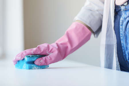 Close-up of woman in rubber gloves using sponge to clean the table