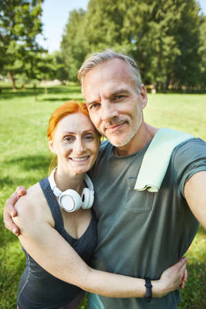 Self-portrait of happy sporty mature couple embracing each other in beautiful park
