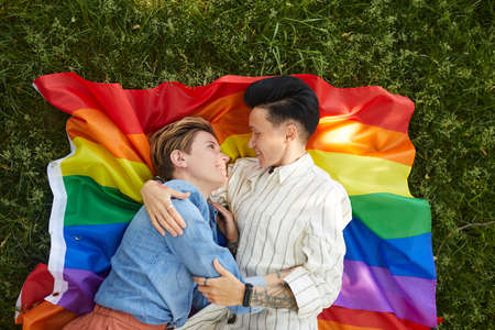 High angle view of two lesbians lying on colored flag and embracing during picnic in the parkの写真素材