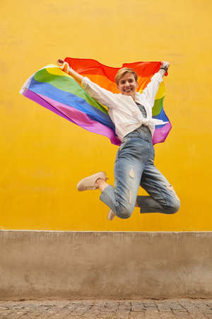 Portrait of young happy woman with colored flag smiling at camera and jumping outdoorsの写真素材
