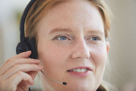 Close-up of red haired woman in headset working with clients at office