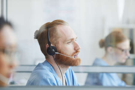 Young bearded man in headphones working in medical call centerの写真素材