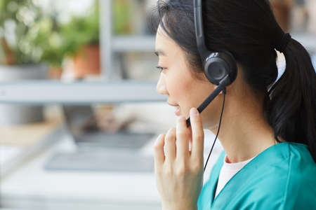 Rear view of Asian young operator in headphones talking to the client she working in customer serviceの写真素材