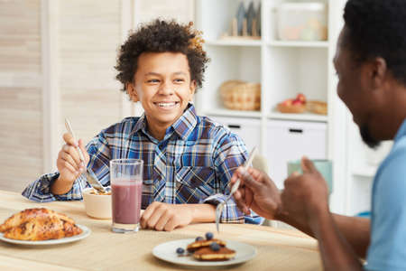 African boy with curly hair smiling to his father while they having breakfast together in the kitchenの写真素材