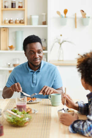 African young father has breakfast together with his son at the table in the kitchen they smiling and talkingの写真素材