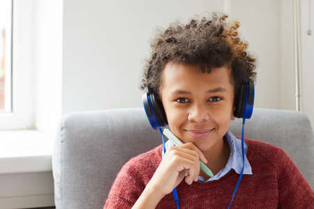 Portrait of African boy with curly hair in headphones listening to music and smiling at camera