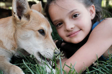 Close-up of cute little girl looking at camera while lying on the grass with the dogの写真素材