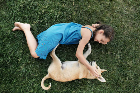 High angle view of little girl lying on the grass with her dog and playing on fresh airの写真素材
