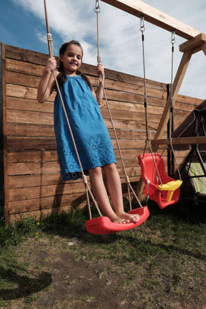 Portrait of happy little girl in blue dress playing outdoors she swingingの写真素材