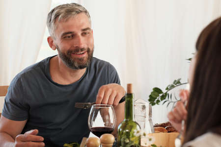 Mature man smiling to his woman while they sitting at the table and having dinner at home