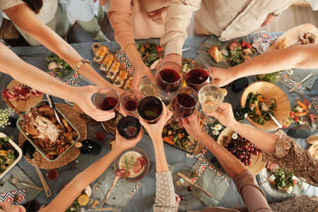 High angle view of group of people holding glasses and toasting with red wine at the table during dinnerの写真素材