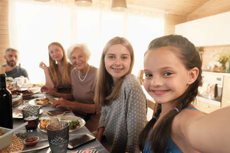 Portrait of little girl smiling and making selfie portrait of her big family while they sitting at the table during dinner at homeの写真素材