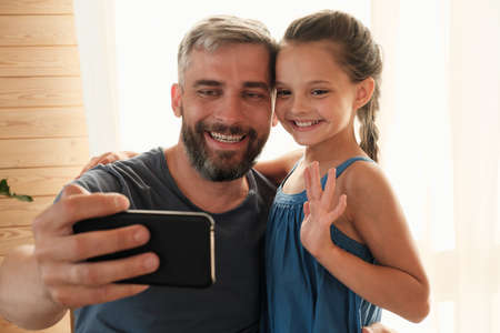 Happy father making selfie portrait on his mobile phone with his little girl they smiling at cameraの写真素材