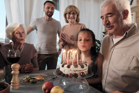 Big happy family celebrating birthday of their father with birthday cake at the table at home
