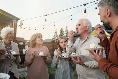 Big family standing in the circle and eating cake together during party on fresh airの写真素材