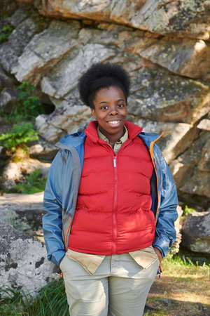 Portrait of African young woman in warm clothing smiling at camera while hiking