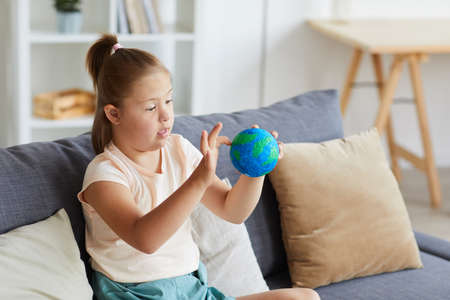 Girl with down syndrome examining the model of Earth planet while sitting on sofa at home