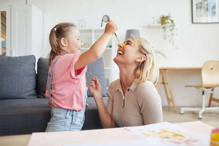 Child with down syndrome painting the face of her mother with paints they are at homeの写真素材