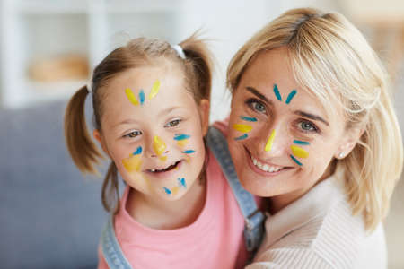 Portrait of happy mother and her daughter with down syndrome with painted faces smiling at cameraの写真素材