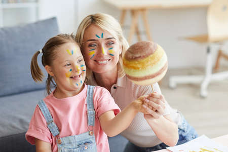 Smiling mother showing her daughter with down syndrome the model of the planetの写真素材