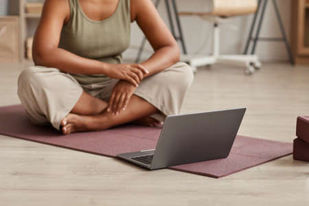 Close-up of woman sitting on exercise mat in front of laptop and watching yoga exercises online at homeの写真素材