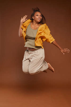 Portrait of African happy woman in fashion clothes jumping against the brown backgroundの写真素材
