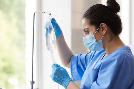 Nurse in mask and in protective gloves preparing dropper for patient at hospital