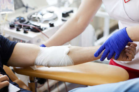 Close-up of patient with bandaged hand donating blood with nurse working with himの写真素材