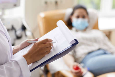 Close-up of female doctor holding medical card and writing prescription for patient at hospitalの写真素材