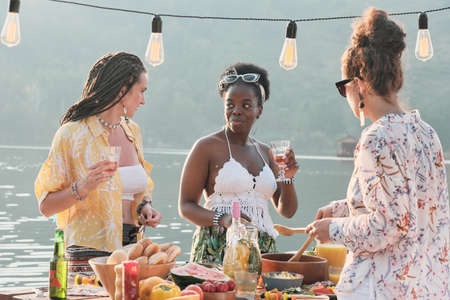 Young beautiful women standing near the dining table and talking to each other they have lunch...