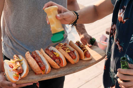 Close-up of young people adding sauce on hot dogs they preparing food for the party outdoorsの写真素材