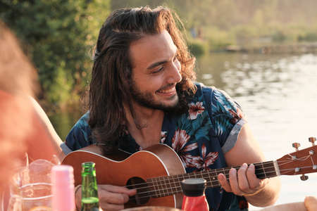 Young smiling man playing guitar for his friends while sitting at the table during party outdoors
