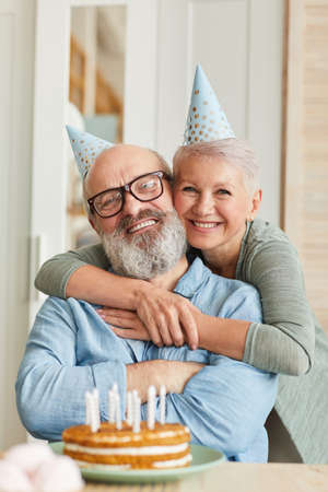 Portrait of happy senior family of two smiling at camera while sitting at the table with cake and celebrating birthdayの写真素材