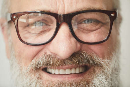 Close-up of senior bearded man in eyeglasses smiling at cameraの写真素材