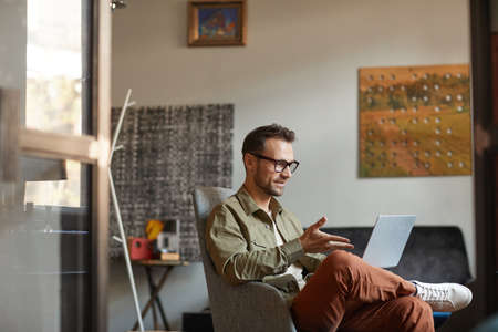 Young man in eyeglasses has a business conference online on laptop computer while sitting at office
