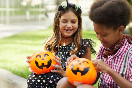 Happy children sitting outdoors and looking at pumpkins bags full of sweetsの写真素材