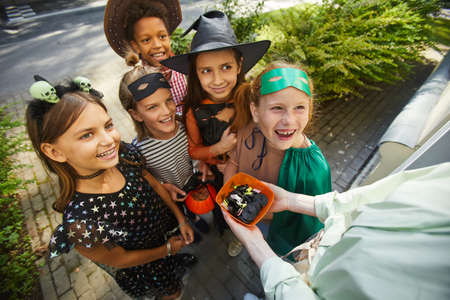 Close-up of woman treating children with sweets on Halloween holiday outdoors