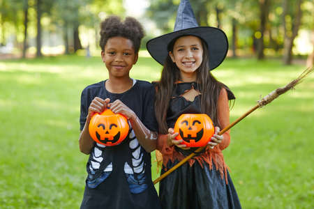 Portrait of two happy friends smiling at camera during Halloween party in the park outdoors