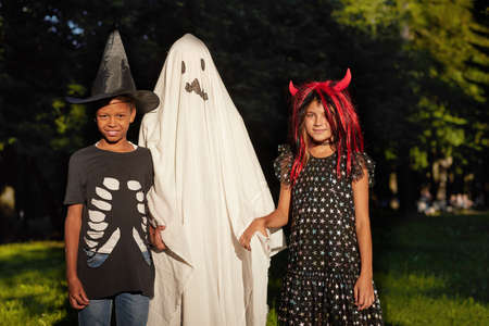 Portrait of children in costumes of witch and ghost smiling at camera during Halloween party...